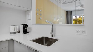 A modern kitchen with a white countertop, stainless steel sink, and a coffee maker.