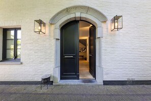 A building entrance with a black door, two wall-mounted lights, and a small table outside. - The haven (St. Genesius-Rode)
