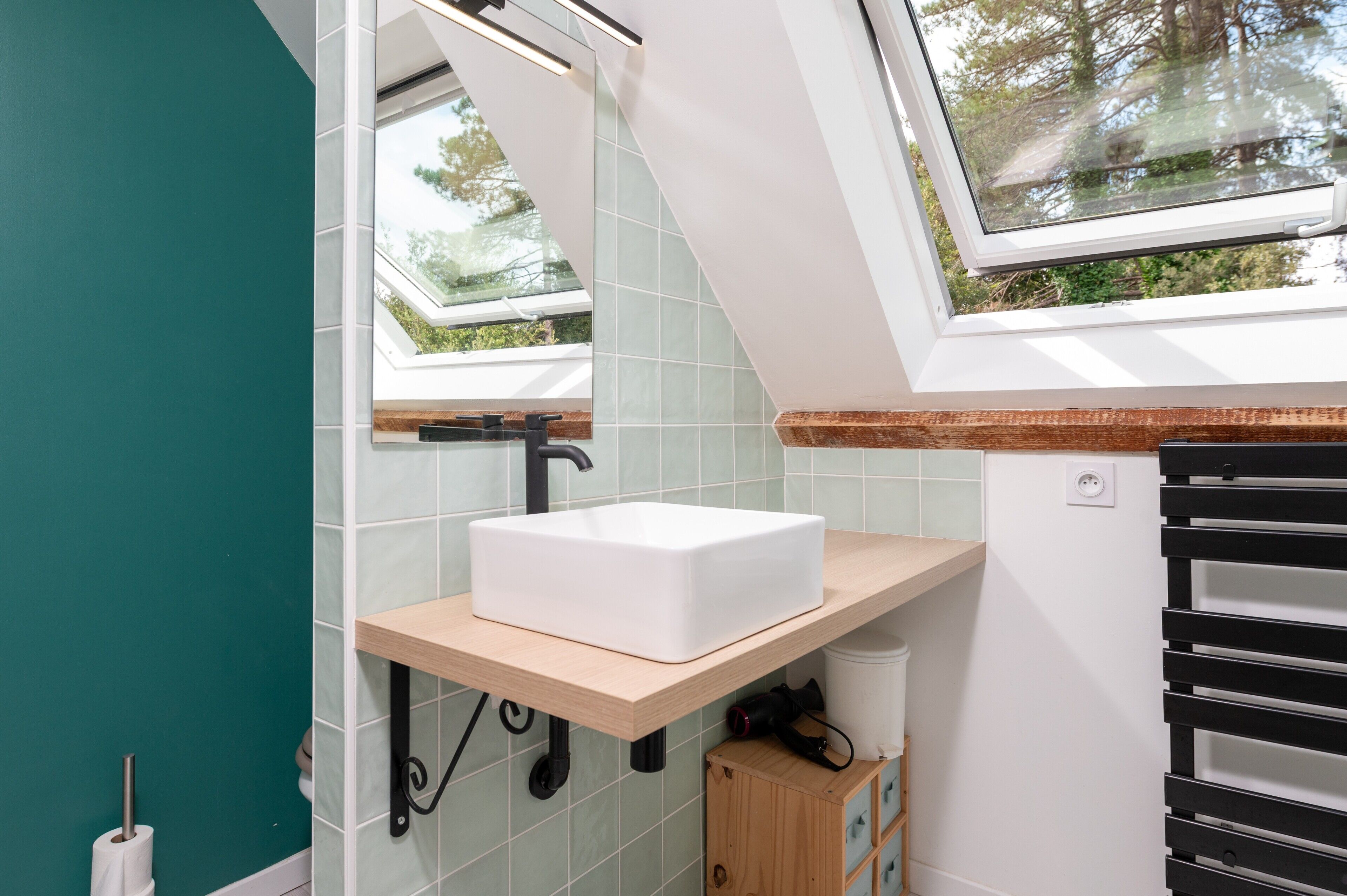 Ein modernes Badezimmer mit Oberlicht, einem weißen Waschbecken und einem Holzregal.
