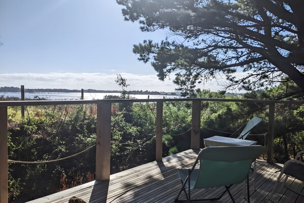 Una terraza de madera con una mesa y sillas, con vista a un cuerpo de agua y vegetación densa.