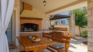 Eine Terrasse im Freien mit einem Ziegelofen, einem Holztisch und Bänken.