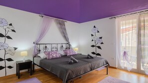 Ein Schlafzimmer mit Bett, Nachttischen, einem Fenster mit Vorhängen und Wandbildern.