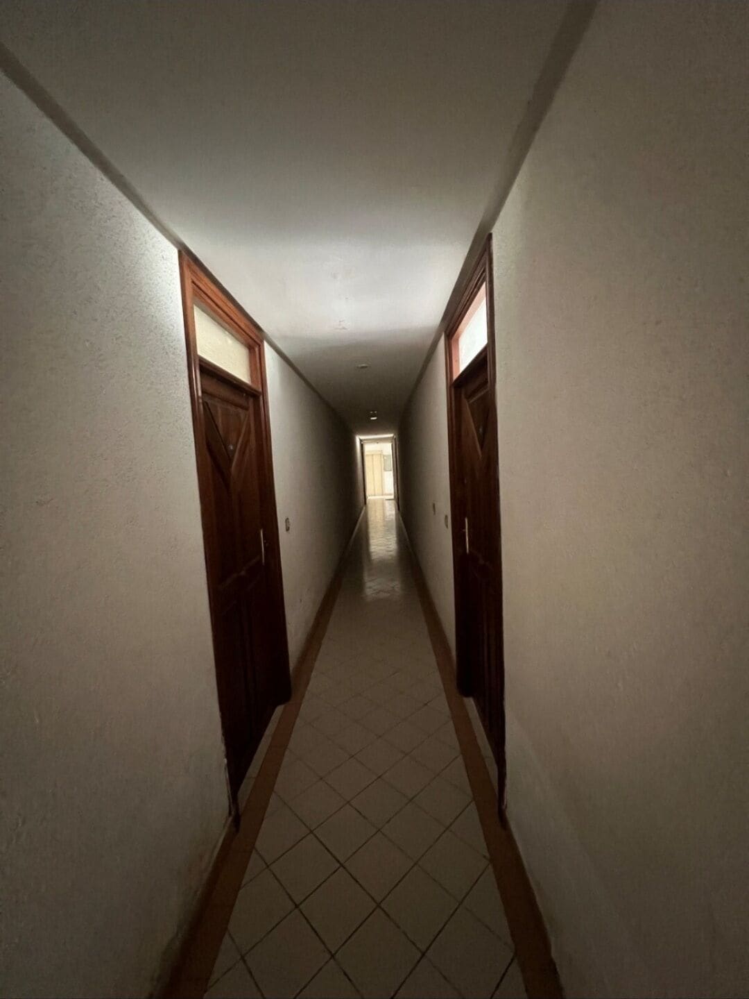 A narrow hallway with tiled flooring and wooden doors on both sides.