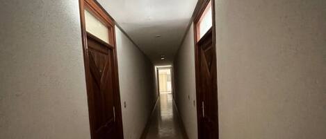 A narrow hallway with tiled flooring and wooden doors on both sides.