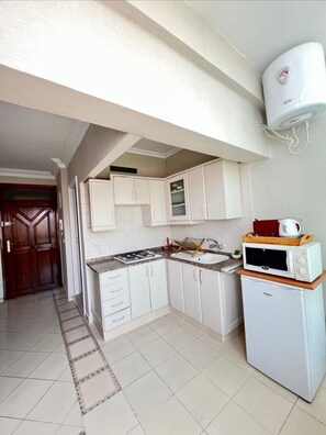 Cocina compacta con armarios blancos, estufa a gas, microondas y horno empotrado.