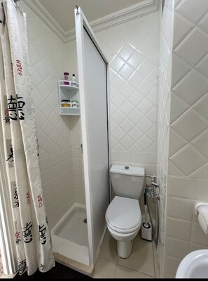 Un baño pequeño y funcional con inodoro, ducha y repisa con artículos de aseo.