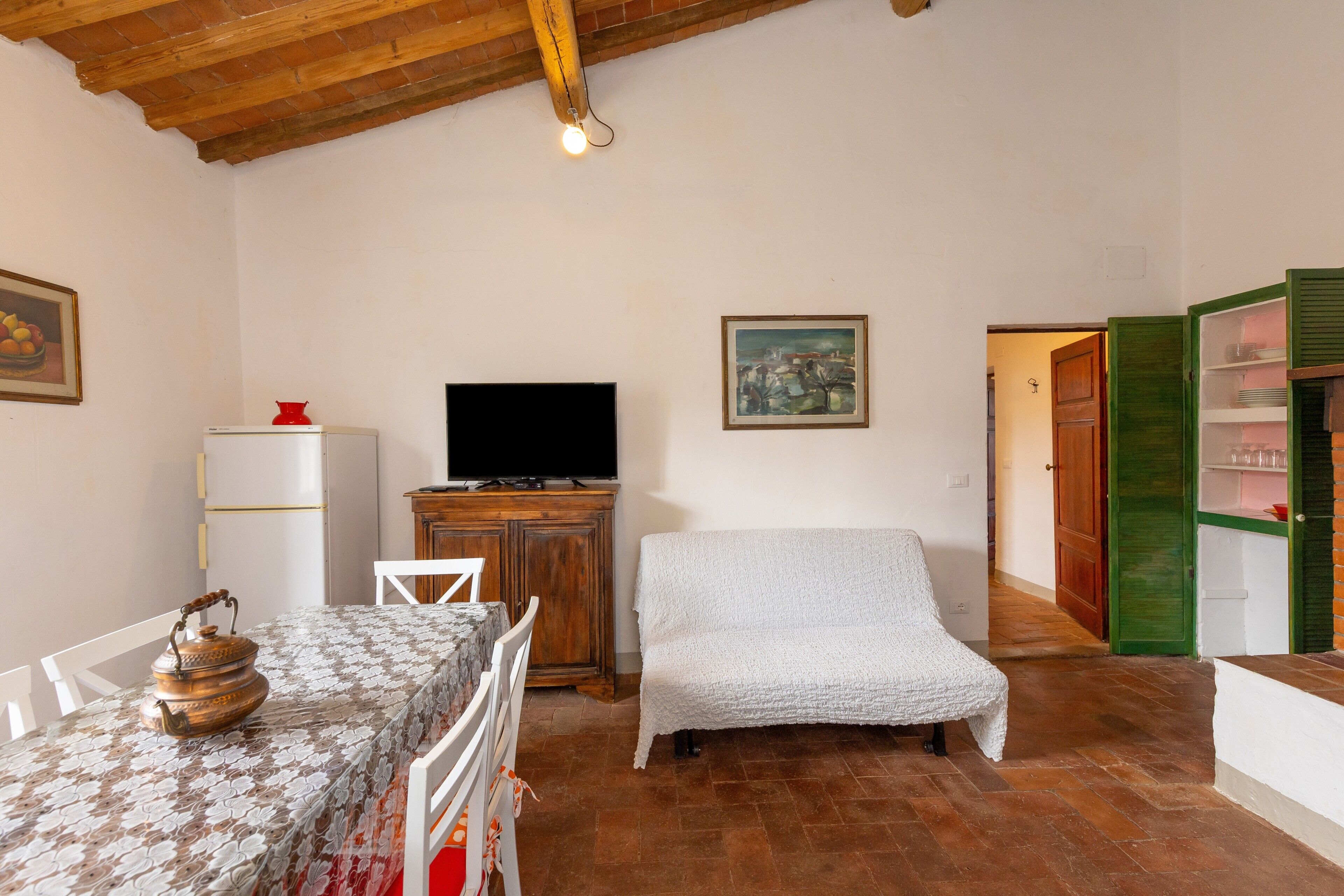 A room with a wooden ceiling, a television, a dining table with chairs, a sofa, and a cabinet.