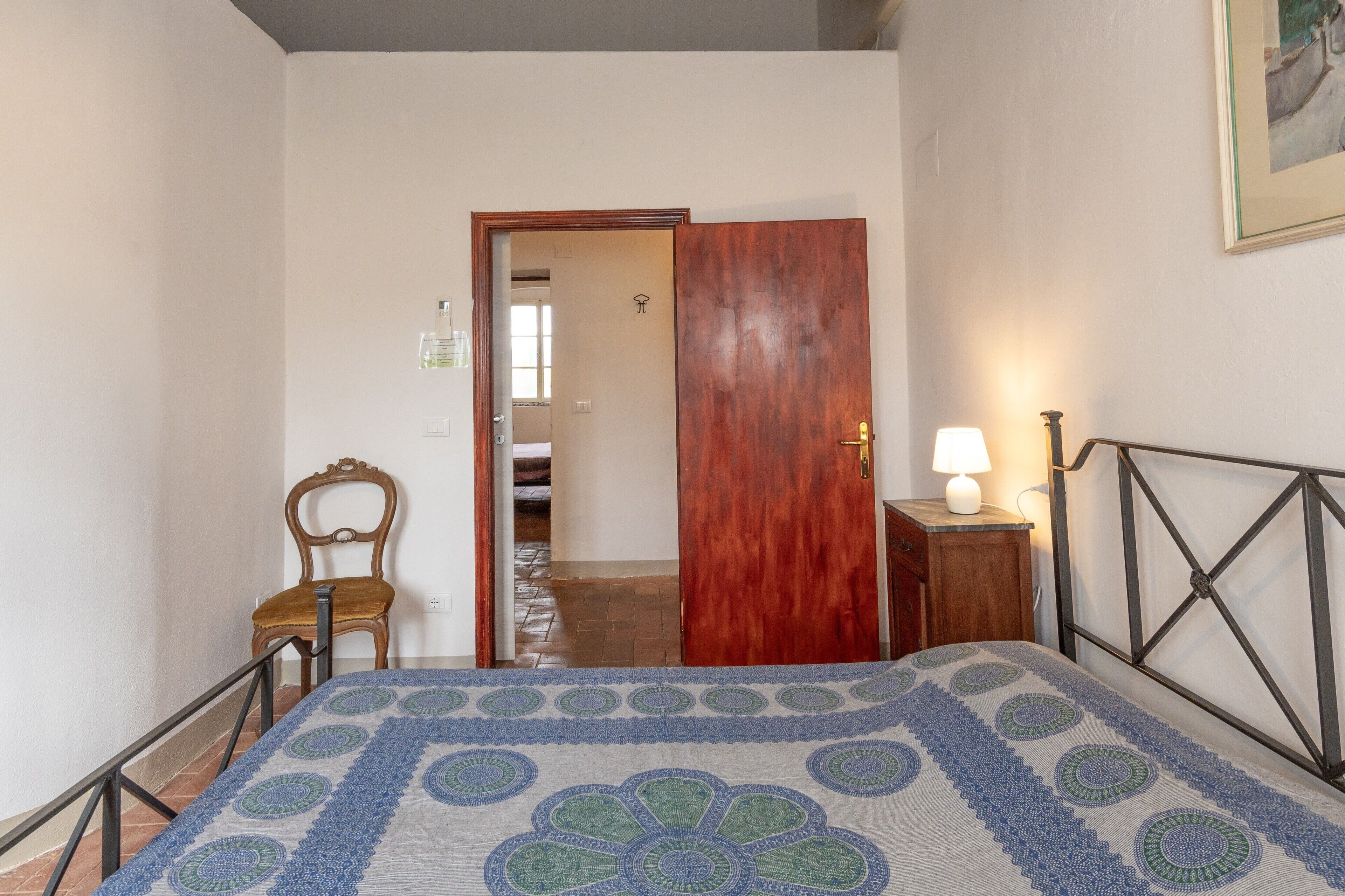 Une chambre à coucher avec un lit, une porte en bois, une chaise, une table de chevet avec une lampe et un tableau encadré au mur.