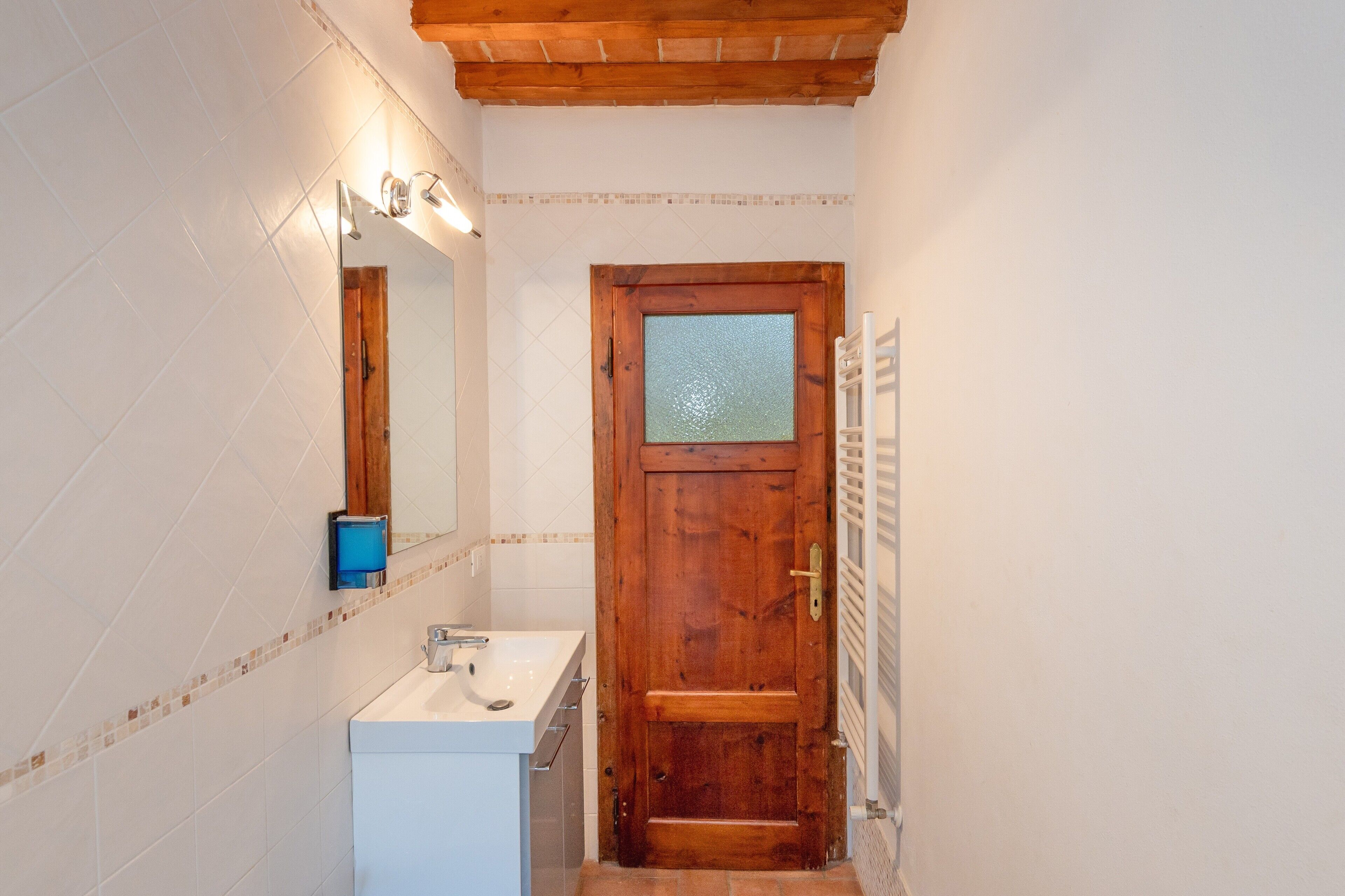 Une salle de bain avec une porte en bois, un lavabo blanc et un miroir.