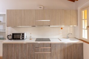 A modern kitchen with wooden cabinets, a microwave, a sink, and a window. - Apartment 'Daria' with Shared Garden and Wi-Fi (Donoratico)