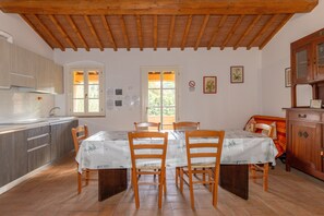 Un coin repas avec des chaises et une table en bois, une cuisine avec des placards, un plafond en bois et une fenêtre donnant sur un paysage verdoyant.