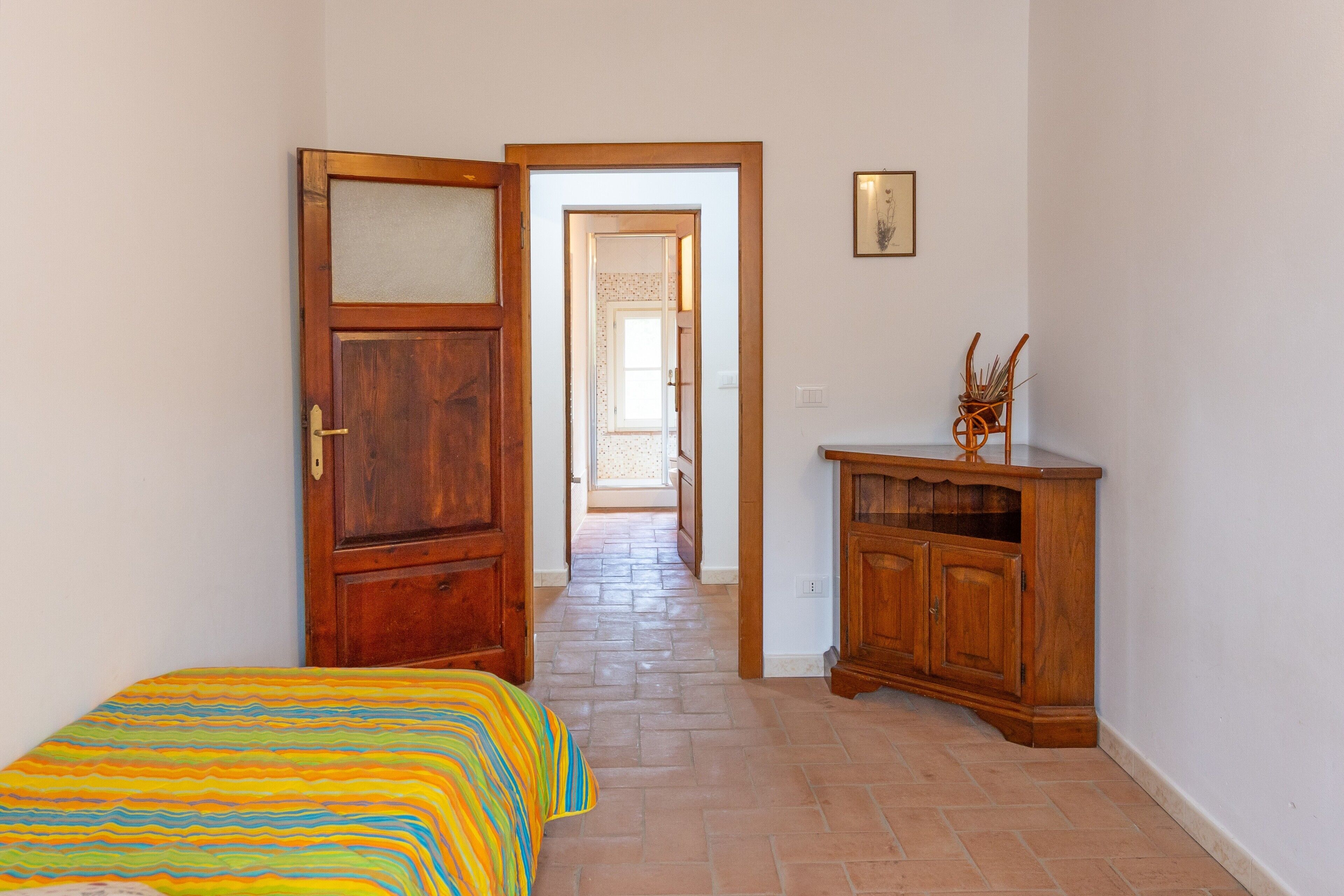 Quarto com uma cama, guarda-roupa de madeira e porta que dá para um corredor.