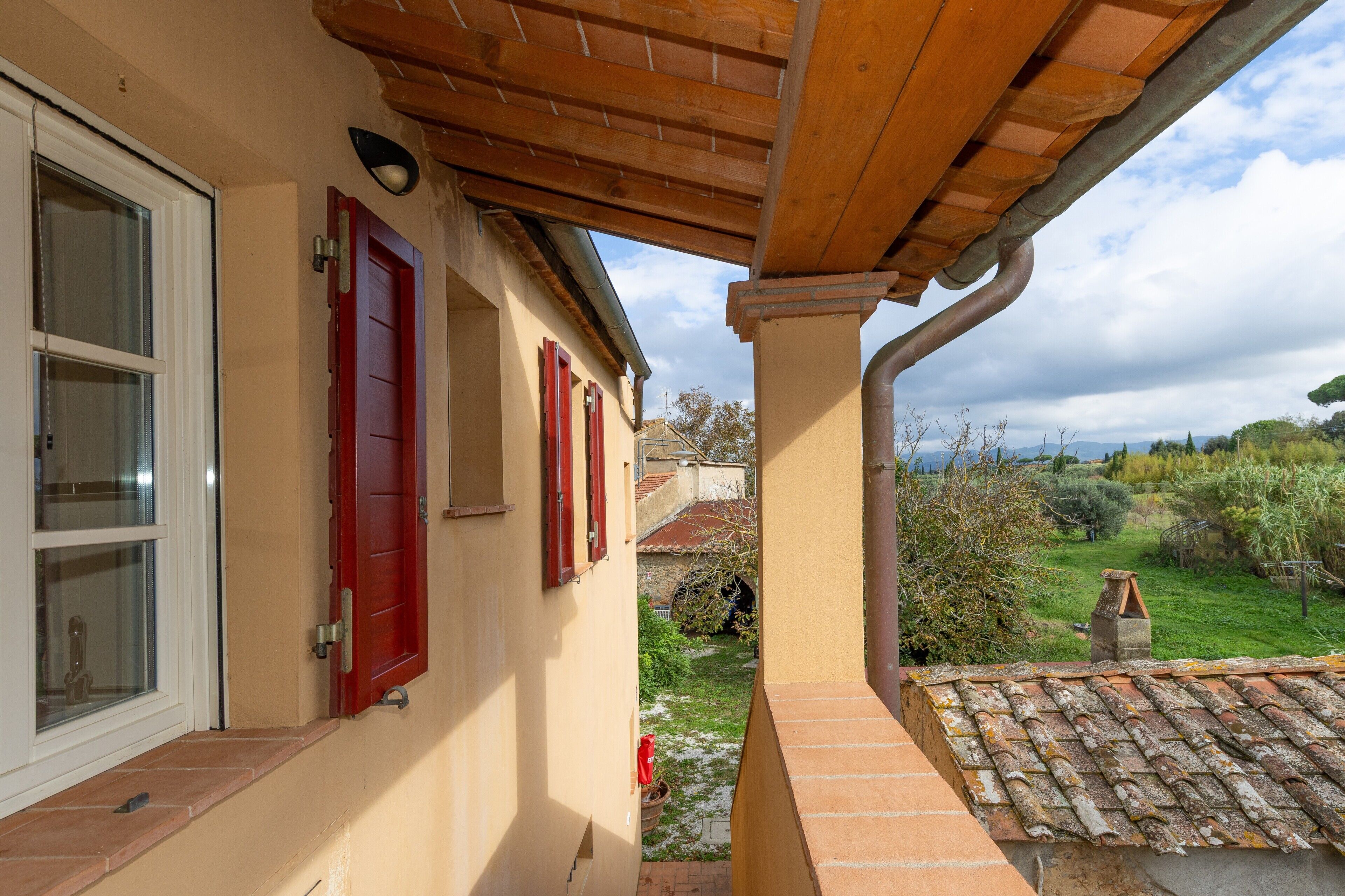 A covered outdoor area with a wooden ceiling, a window with a white frame, and a red door.