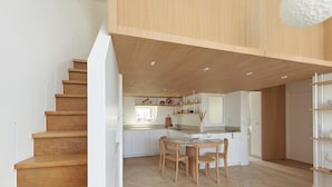 Une cuisine moderne avec des meubles en bois, un coin repas comprenant une table et des chaises, et un escalier menant à l’étage supérieur.