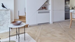 Un intérieur moderne avec un escalier en bois, un coin cuisine et un espace repas comprenant une table et des chaises en marbre.