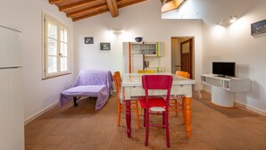 Un espace repas comprenant une table et des chaises, un téléviseur, ainsi qu’un coin cuisine avec des placards et une fenêtre.