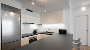 A modern kitchen with white cabinets, a stainless steel refrigerator, a microwave, and a black countertop. - LIV Athinum 1 - Luxury Apartment 1B (Athens)