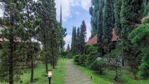 A pathway lined with trees and a stone pavement leading to a building with a red-tiled roof. - Grand Panorama Lembang (Lembang)