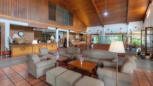 A spacious lobby with a high ceiling, wooden paneling, a reception desk, comfortable seating, and a view of the outdoors. - Grand Panorama Lembang (Lembang)
