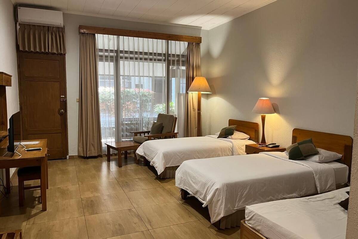 Quarto de hotel com duas camas, uma escrivaninha, uma cadeira e uma televisão.