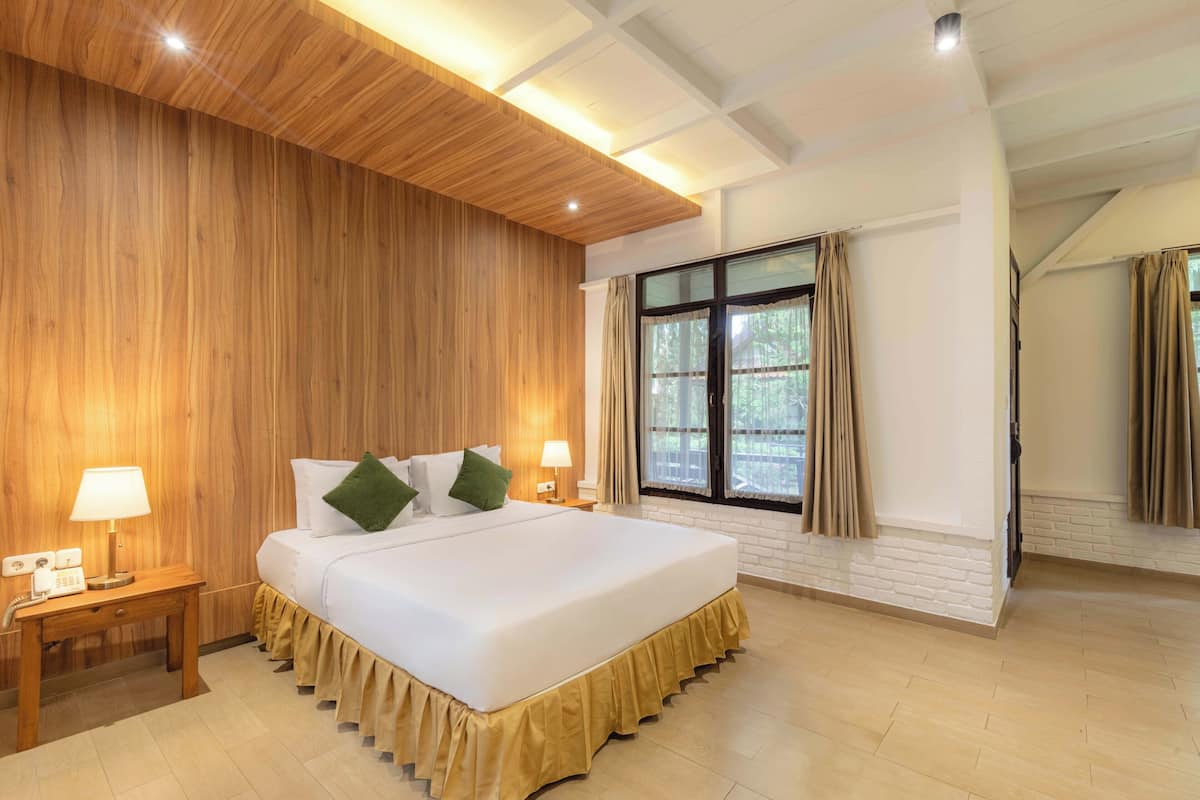 Quarto de hotel com uma cama grande, painéis de madeira nas paredes, uma janela com cortinas e teto de madeira.