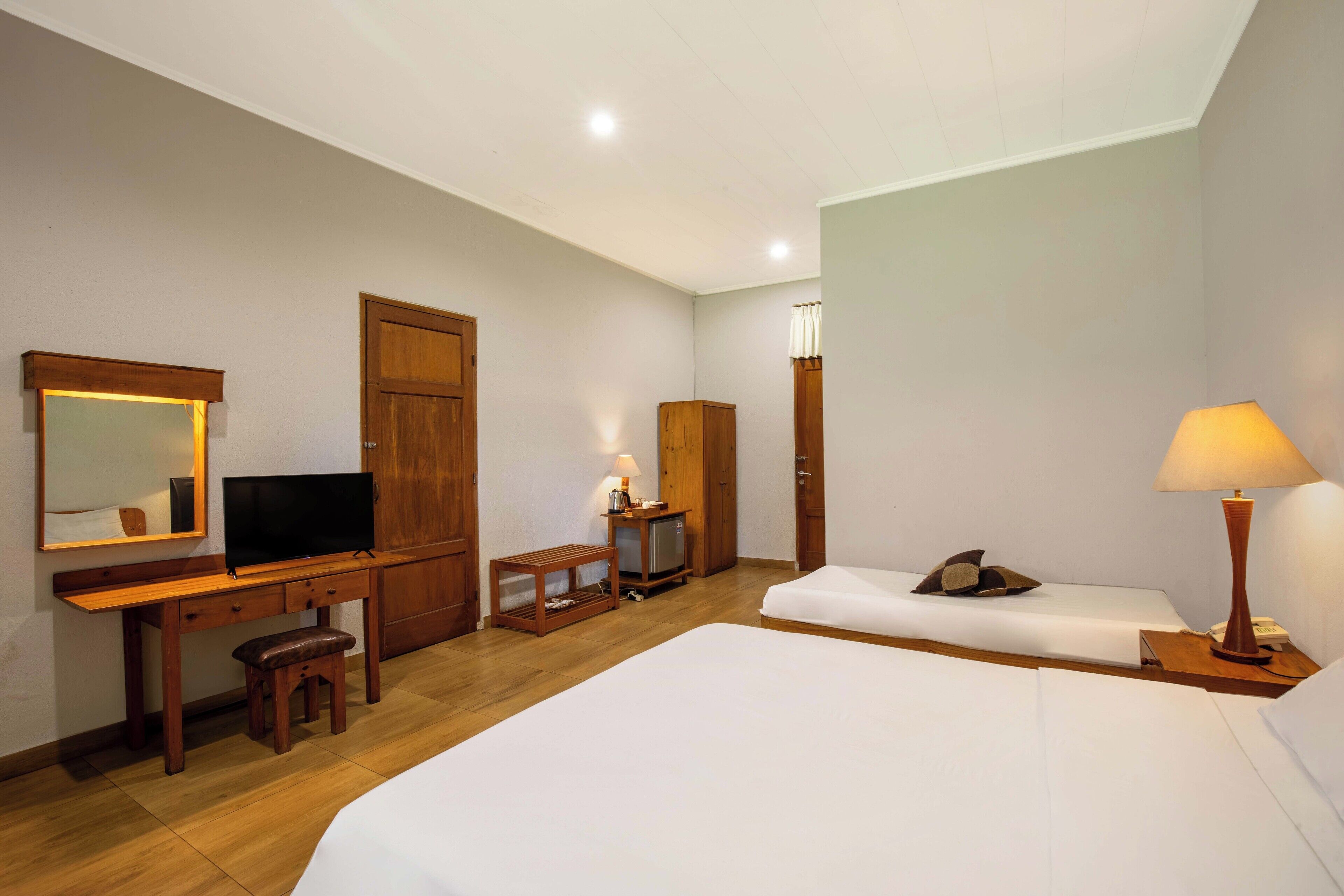 Una habitación de hotel con un escritorio de madera, un televisor, una cama y una mesita de noche con una lámpara.