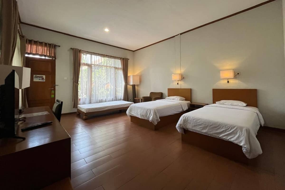 Quarto de hotel com duas camas, uma escrivaninha, uma cadeira, janela com cortinas e luminárias fixadas na parede.
