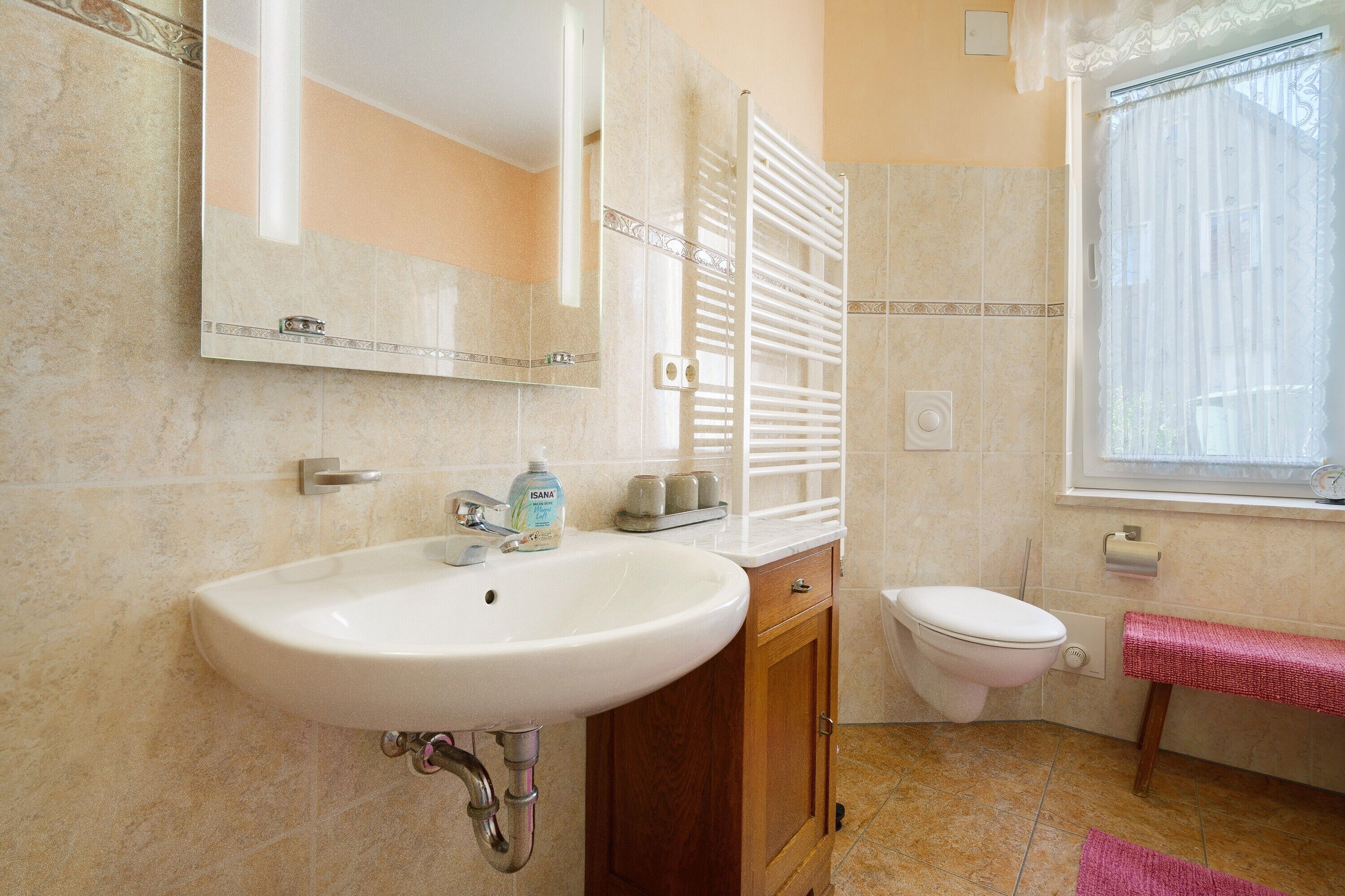 Baño con lavamanos, espejo, inodoro y ventana con cortinas.