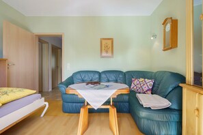 Une pièce avec un canapé en cuir vert, une petite table en bois, un lit avec un oreiller jaune, un tableau encadré accroché au mur et une armoire en bois.