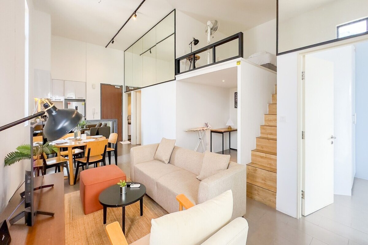 A modern living room with a sofa, ottoman, and a dining area with a table and chairs.
