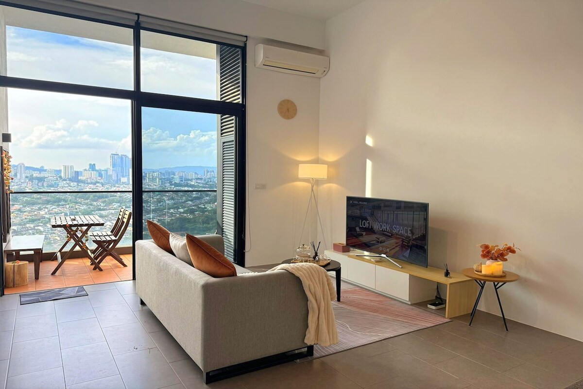 A modern living room with a sofa, a TV, a table, and a view of a cityscape through large windows.