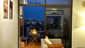 A modern living room with a city view, a sofa, a small table with flowers, and a bench.