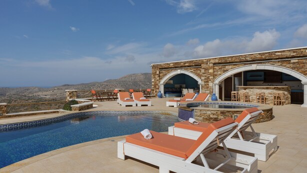 A poolside area with lounge chairs, a bar, and a view of the mountains. - Country House 'Faith - Ios' with Sea View, Wi-Fi and Air Conditioning (ΙΟΣ)