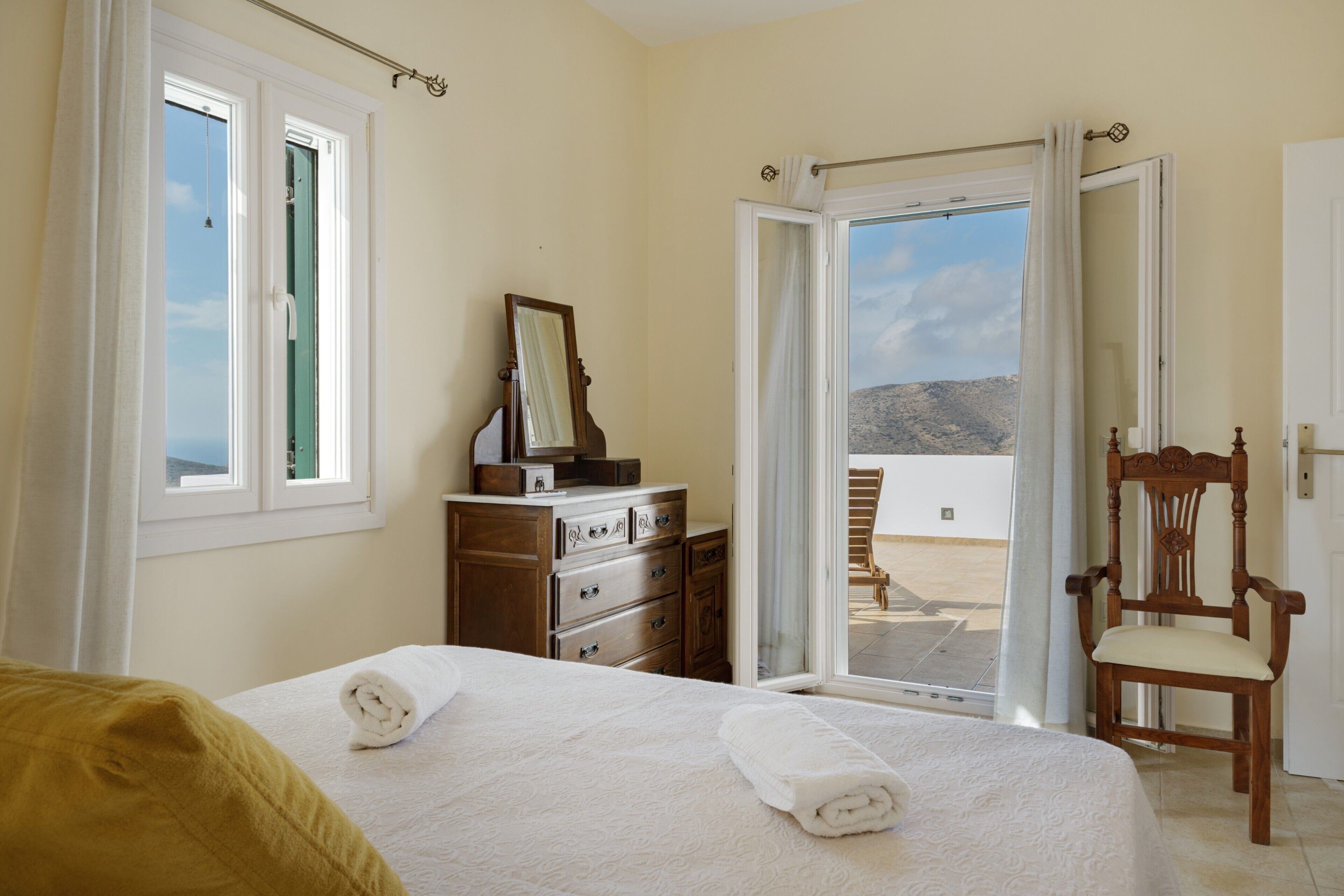 A bedroom with a bed, a wooden dresser, a chair, and a sliding glass door leading to an outdoor area.