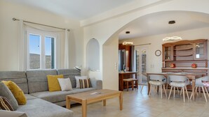 A living room with a sofa, coffee table, and dining area with chairs. - Country House 'Faith - Ios' with Sea View, Wi-Fi and Air Conditioning (ΙΟΣ)