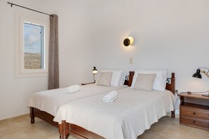 Een tweepersoonsbed met twee kussens, een nachtkastje met een lamp, en een raam met uitzicht op een landschap.