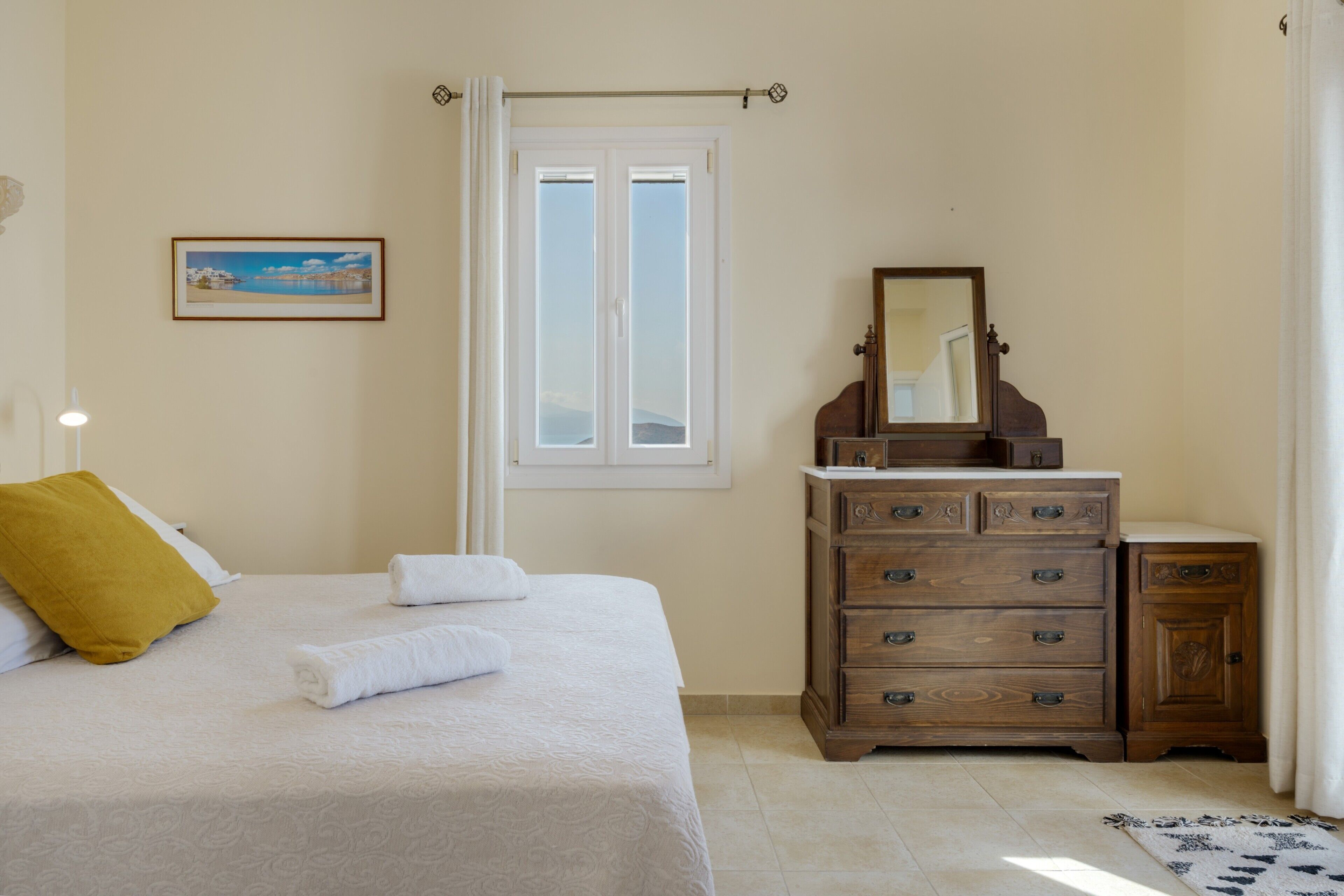 A bedroom with a bed, a dresser, a mirror, a window, and a picture on the wall.