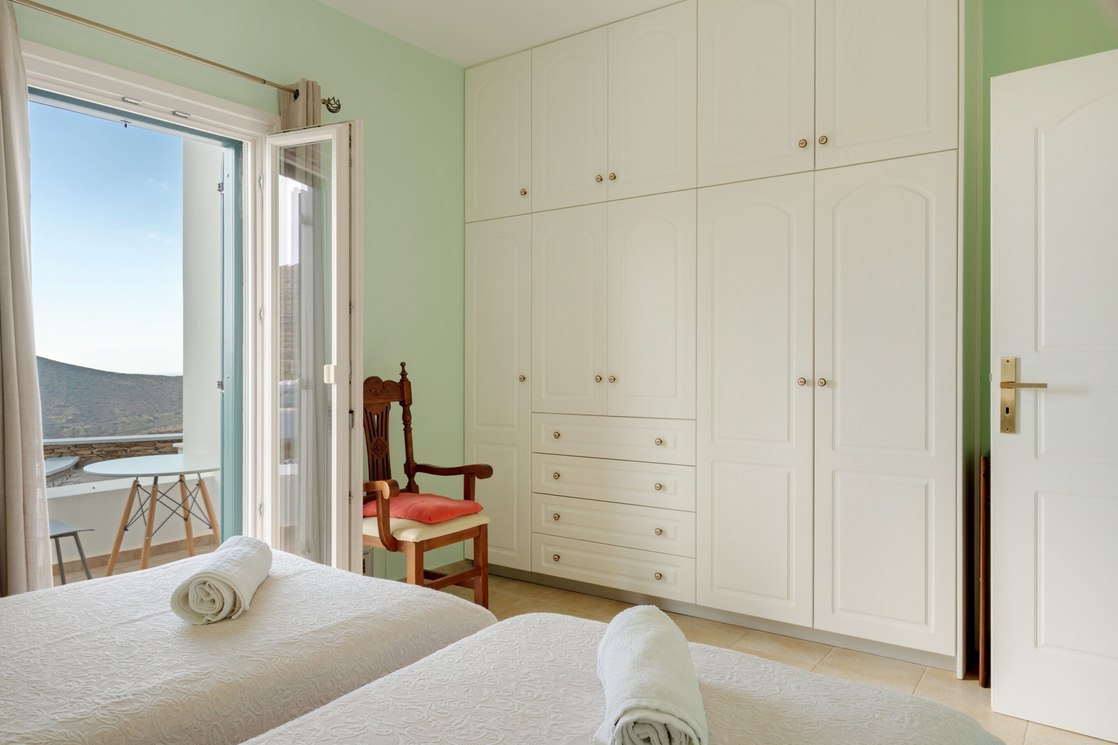 Une chambre avec deux lits, une armoire, une chaise et une vue sur l’extérieur.