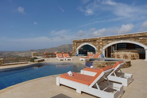 A poolside area with lounge chairs, a bar, and a view of the mountains. - Country House 'Hope - Ios' with Sea View, Wi-Fi and Air Conditioning (ΙΟΣ)