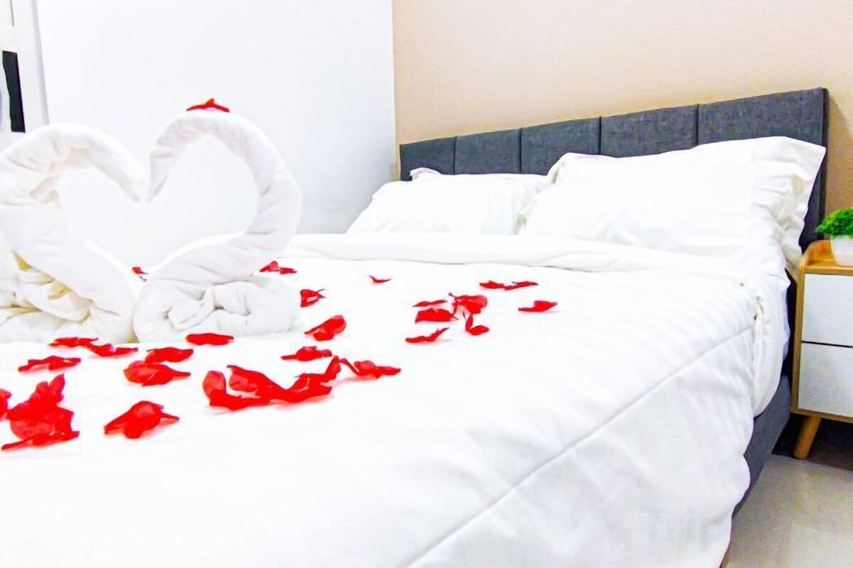 Un lit avec du linge de lit blanc, une disposition de serviettes en forme de cœur et des pétales de rose éparpillés.