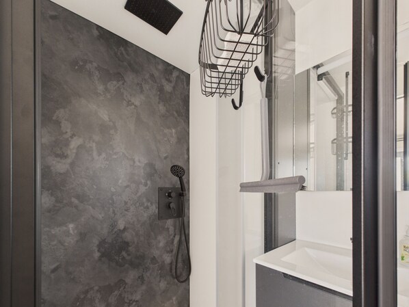 Een moderne badkamer met een grijze, gestructureerde wand, een douche met handdouche en een spiegel met plankje.
