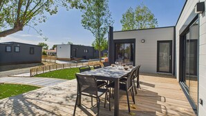 Een modern buitenterras met een houten dek, een eettafel met stoelen, en een gebouw met grote ramen en een deur.