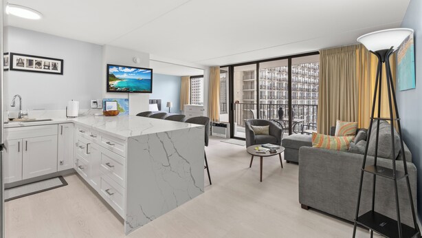 A modern living room with a marble island, grey sofa, and a flat-screen TV. - Waikiki Banyan 1BR (Honolulu)