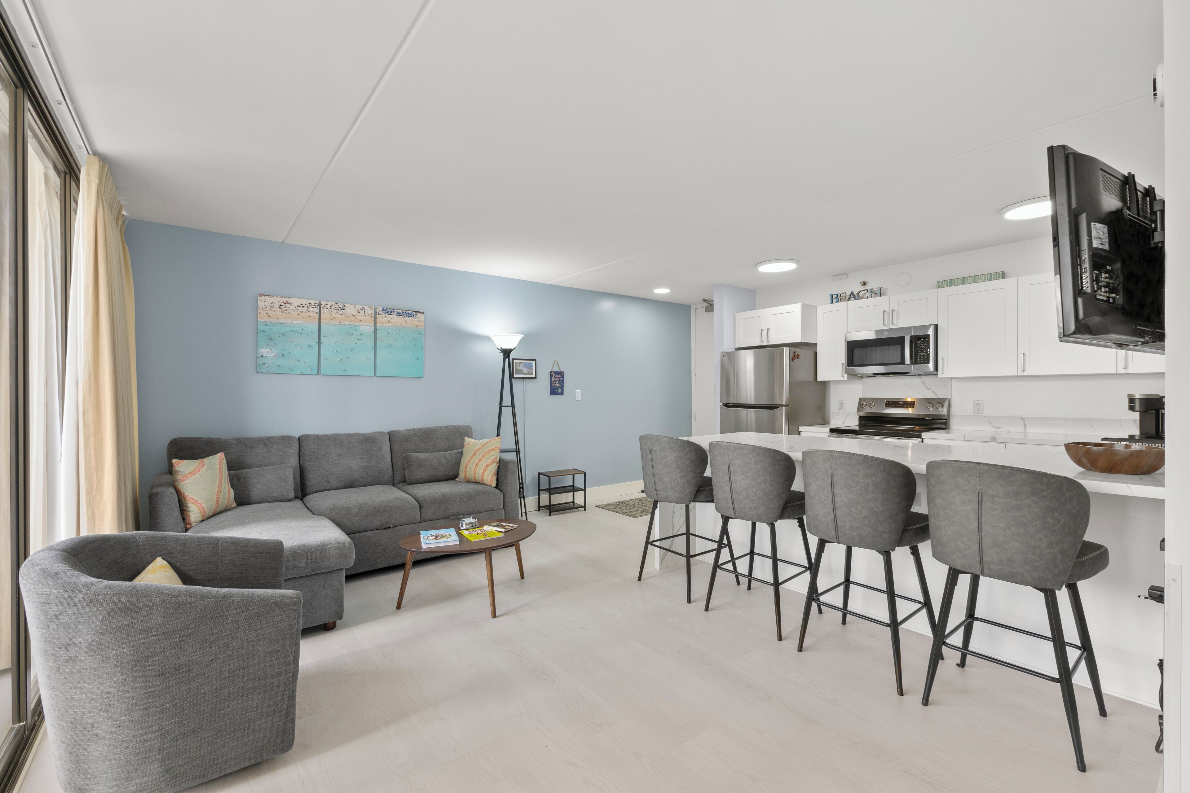 A modern living room with a grey sofa, a coffee table, and a kitchen area with white cabinets and a microwave.