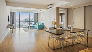 A modern apartment with a dining area, a sofa, and a large window offering a city view.