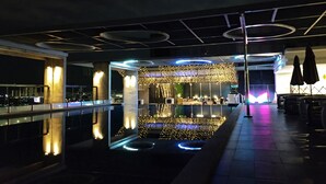 A modern indoor pool area with a bar and lounge seating, illuminated by ambient lighting and string lights.