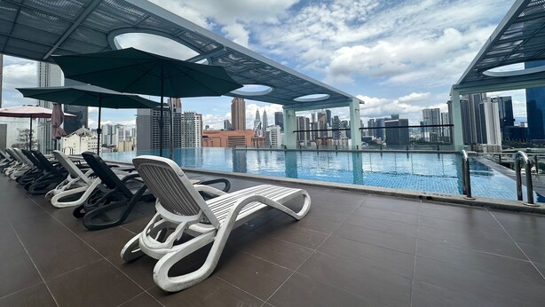 A rooftop pool area with lounge chairs and umbrellas, overlooking a city skyline.