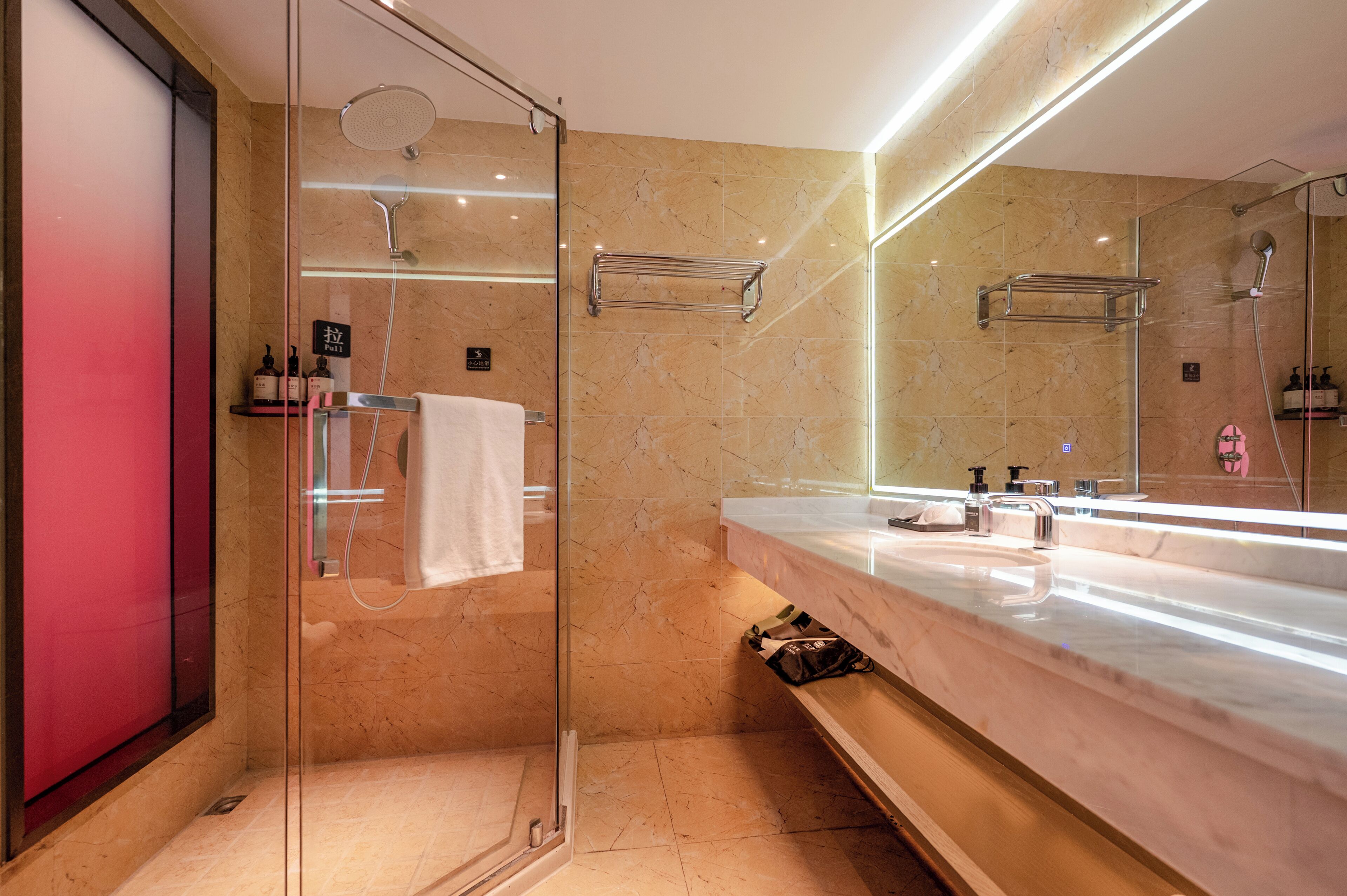 A modern bathroom with a glass-enclosed shower, a marble-tiled wall, a large mirror, and a marble countertop.