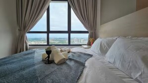 Une chambre d’hôtel dotée d’une grande fenêtre, d’un lit avec du linge de lit blanc, d’un tapis bleu à motifs et d’une petite table sur laquelle se trouvent un vase et une plante.