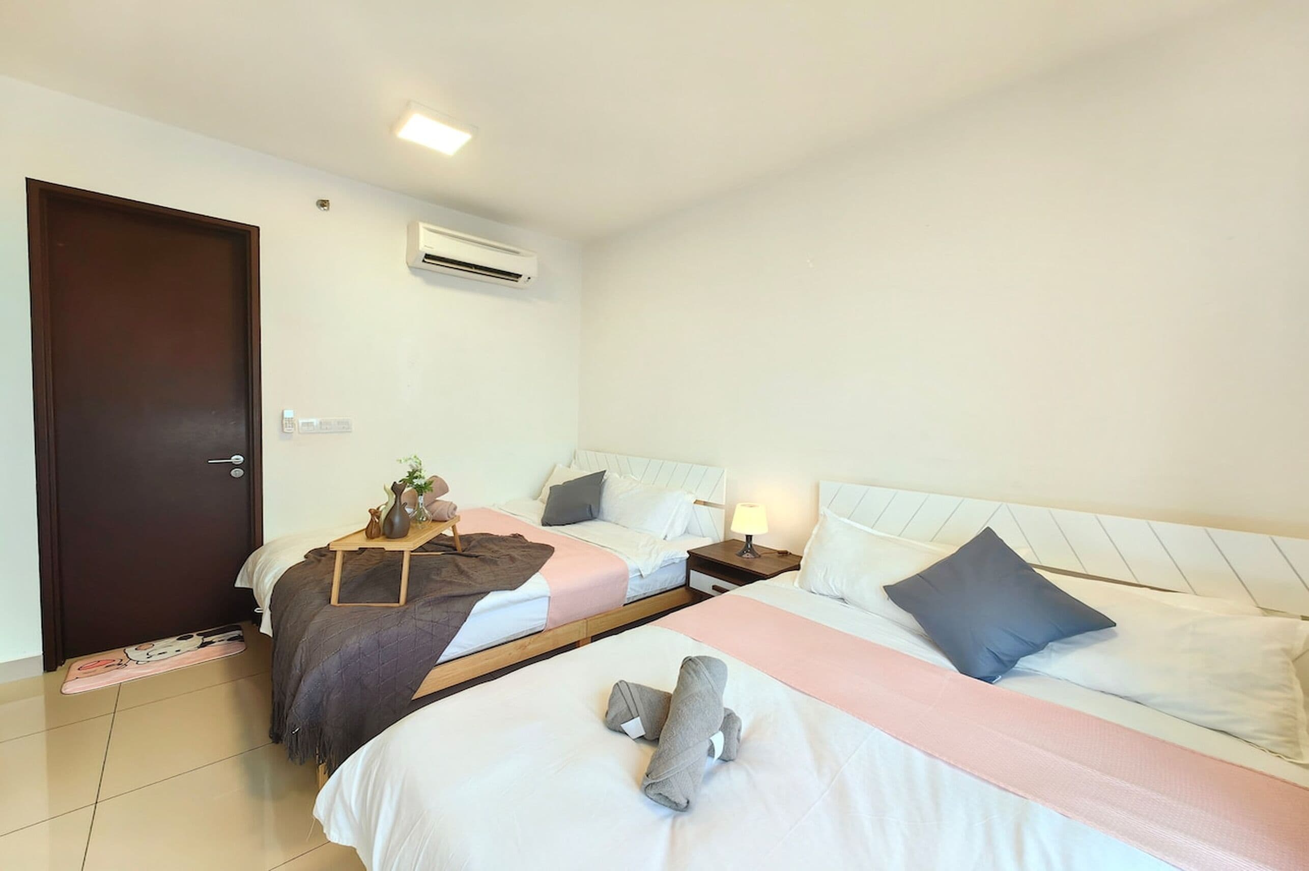 Ein Hotelzimmer mit zwei Betten, einem Holznachttisch, einem kleinen Tisch mit Lampe und einer Klimaanlage an der Wand.